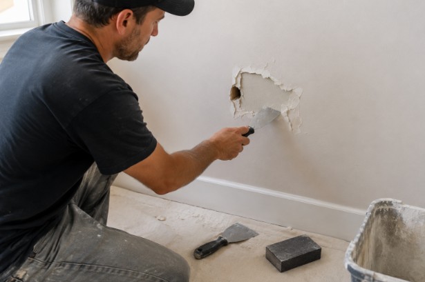Contractor preparing a damaged wall for drywall repair.