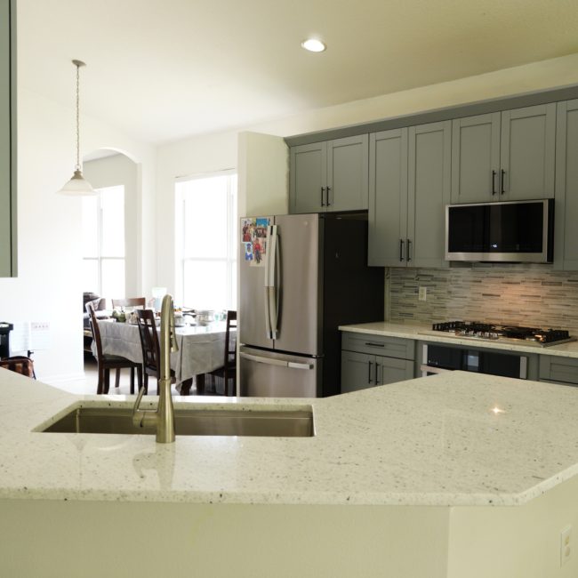 Renovated kitchen featuring gray cabinets, speckled granite, and a matching tile backsplash.