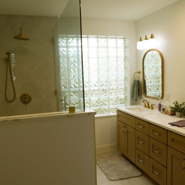 Luxury bathroom remodel with a walk-in glass shower, gold fixtures, and double vanity.