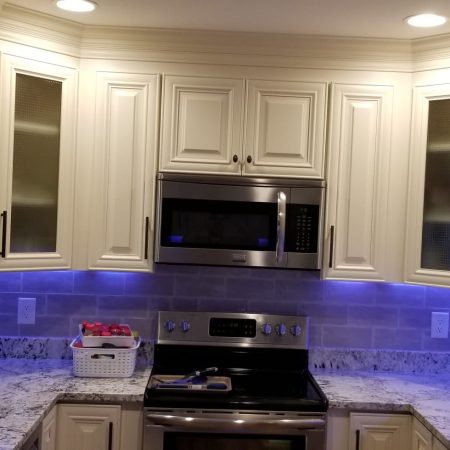 Modern kitchen with white cabinets and blue under-cabinet lighting.