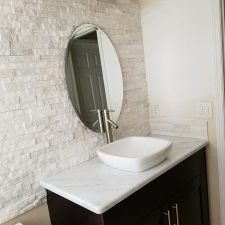 Modern bathroom sink with oval mirror and textured white wall.