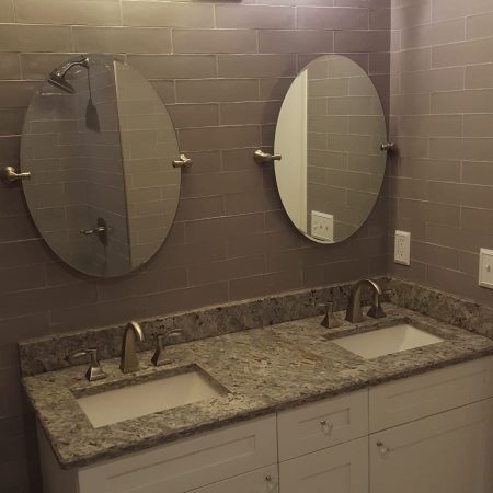 Modern double sink bathroom vanity with oval mirrors and granite countertop.